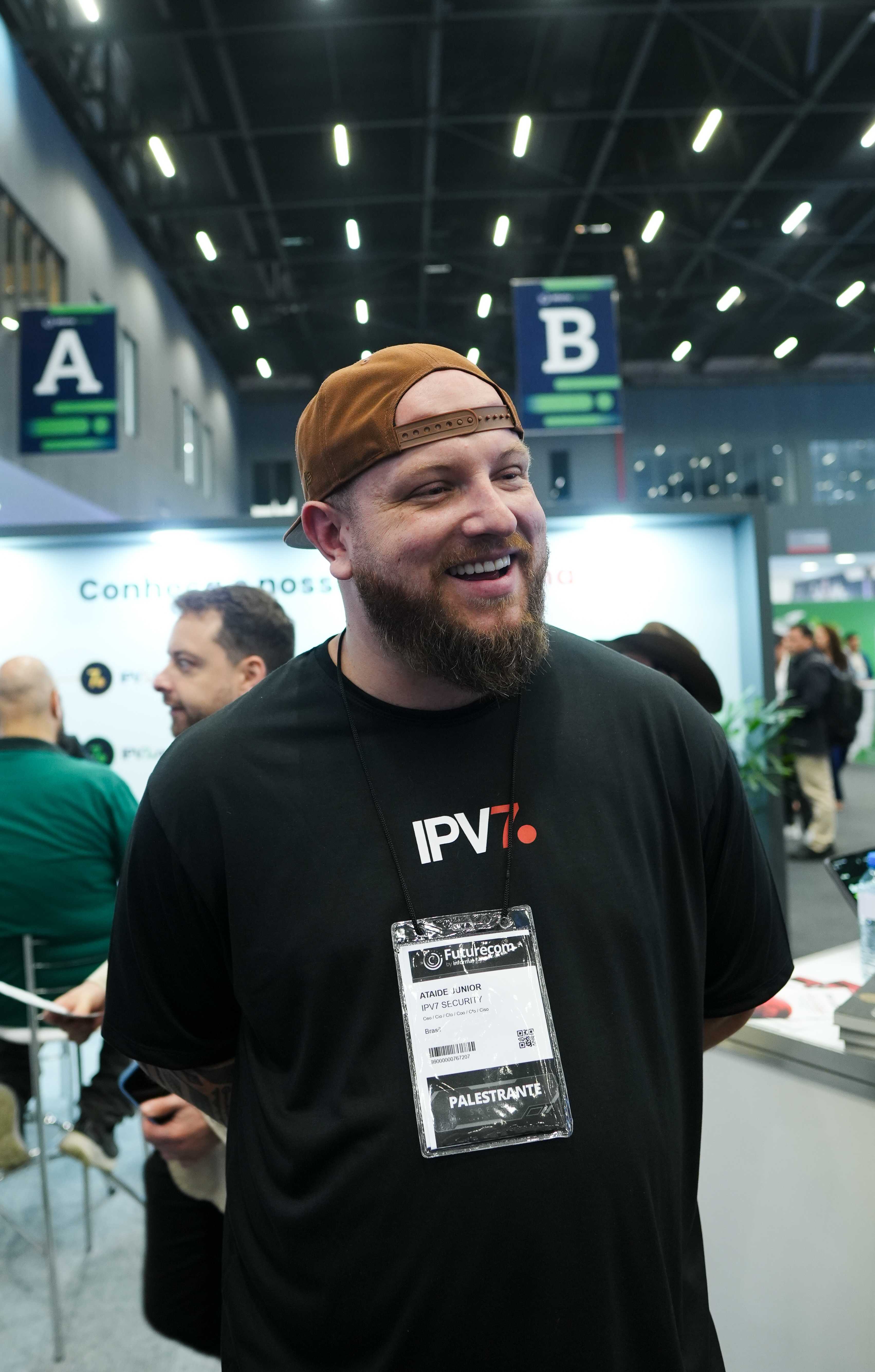 Ataide Junior sorrindo no Futurecom, com crachá de palestrante e camiseta da IPV7